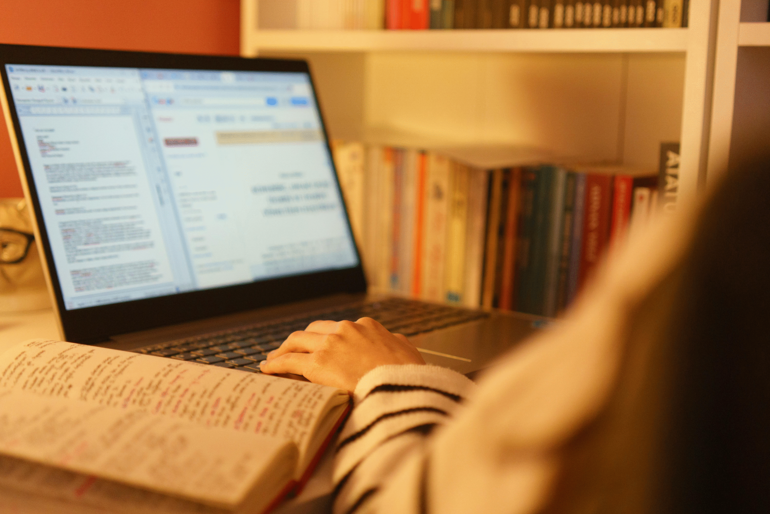 A student studies at a desk using a laptop while reviewing notes from an open notebook. The image highlights a flexible learning environment with digital study resources, self-paced education, and focused academic preparation in a home setting.